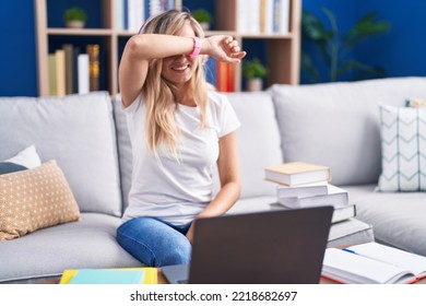 Young Blonde Woman Studying Using Computer Laptop At Home Covering Eyes With Arm Smiling Cheerful And Funny. Blind Concept. 