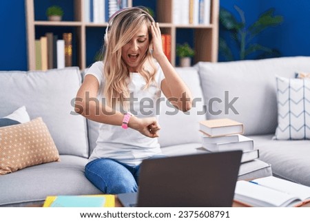 Young blonde woman studying using computer laptop at home looking at the watch time worried, afraid of getting late 
