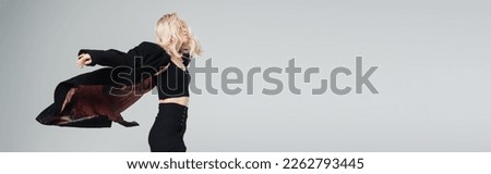 young blonde woman in stylish black outfit jumping isolated on grey, banner