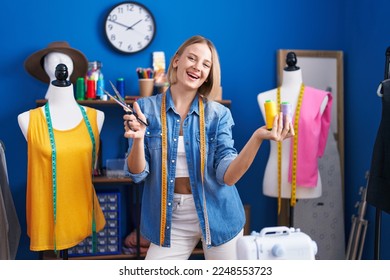 Young blonde woman tailor smiling confident holding scissors and thread at sewing studio - Powered by Shutterstock