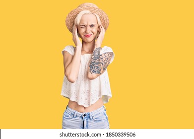 Young blonde woman with tattoo wearing summer hat covering ears with fingers with annoyed expression for the noise of loud music. deaf concept.  - Shutterstock ID 1850339506