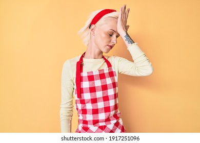 Young Blonde Woman With Tattoo Wearing Professional Baker Apron Surprised With Hand On Head For Mistake, Remember Error. Forgot, Bad Memory Concept. 