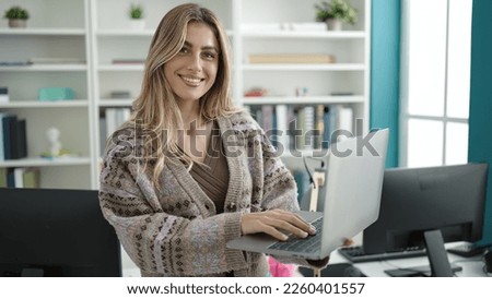 Young blonde woman teacher using laptop standing at library university