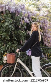 Young Blonde Woman In Trendy Outfit Near Bicycle And Blooming Tree In Turkey