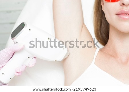 A young blonde woman undergoes the procedure of laser hair removal of her armpits in a beauty clinic