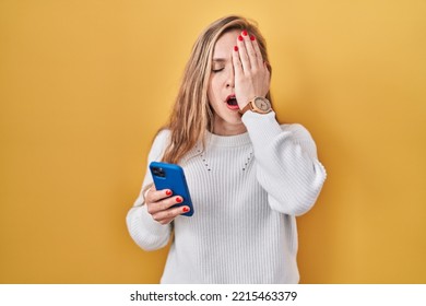 Young Blonde Woman Using Smartphone Typing Message Yawning Tired Covering Half Face, Eye And Mouth With Hand. Face Hurts In Pain. 