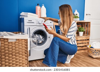 Young blonde woman using smartphone and washing clothes at laundry room - Powered by Shutterstock