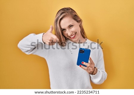Young blonde woman using smartphone typing message pointing fingers to camera with happy and funny face. good energy and vibes. 