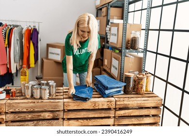 Young blonde woman volunteer smiling confident folding jeans to donate at charity center - Powered by Shutterstock