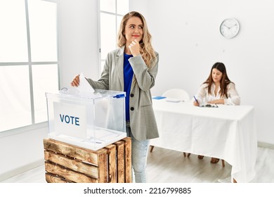 Young Blonde Woman Voting Putting Envelop In Ballot Box Serious Face Thinking About Question With Hand On Chin, Thoughtful About Confusing Idea 