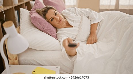 Young blonde woman watching tv lying on bed tired at bedroom - Powered by Shutterstock