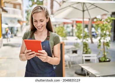 Young blonde woman wearing apron using touchpad at coffee shop - Powered by Shutterstock