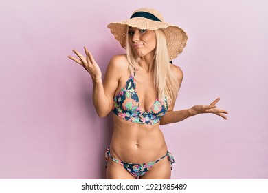 Young blonde woman wearing bikini and summer hat clueless and confused with open arms, no idea and doubtful face. 