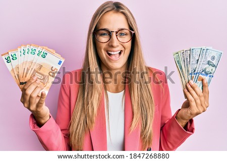 Young blonde woman wearing business style holding dollars and euros banknotes smiling and laughing hard out loud because funny crazy joke. 