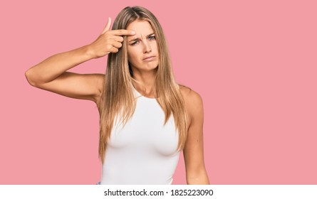 Young Blonde Woman Wearing Casual Style With Sleeveless Shirt Pointing Unhappy To Pimple On Forehead, Ugly Infection Of Blackhead. Acne And Skin Problem 