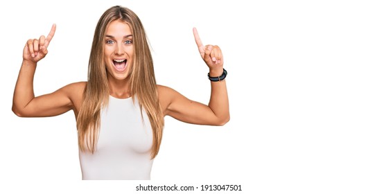 Young Blonde Woman Wearing Casual Style With Sleeveless Shirt Smiling Amazed And Surprised And Pointing Up With Fingers And Raised Arms. 