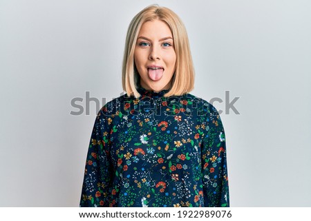 Young blonde woman wearing casual clothes sticking tongue out happy with funny expression. emotion concept. 
