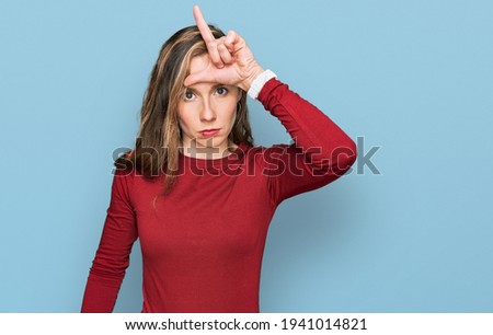 Young blonde woman wearing casual clothes making fun of people with fingers on forehead doing loser gesture mocking and insulting. 