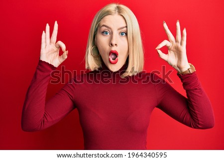 Young blonde woman wearing casual clothes looking surprised and shocked doing ok approval symbol with fingers. crazy expression 