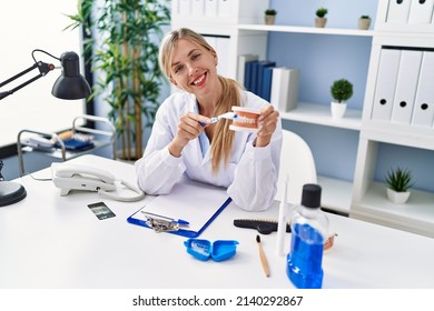 Young Blonde Woman Wearing Dentist Uniform Using Teethbrush At Clinic