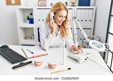 Young Blonde Woman Wearing Dentist Uniform Speaking On The Phone At Dental Clinic