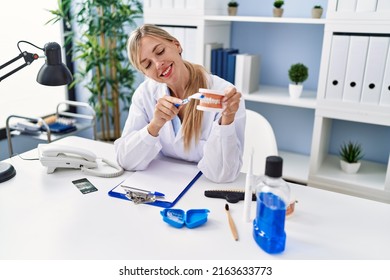 Young Blonde Woman Wearing Dentist Uniform Using Teethbrush At Clinic