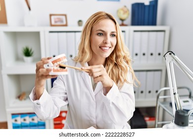 Young Blonde Woman Wearing Dentist Uniform Using Toothbrush At Dental Clinic