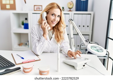 Young Blonde Woman Wearing Dentist Uniform Speaking On The Phone At Dental Clinic