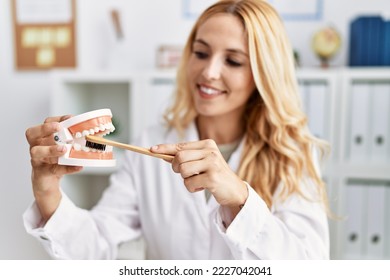 Young Blonde Woman Wearing Dentist Uniform Using Toothbrush At Dental Clinic