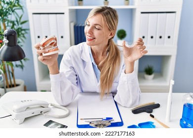 Young Blonde Woman Wearing Dentist Uniform Holding Brackets And Invisible Aligneer At Clinic