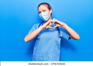 Young blonde woman wearing doctor uniform and medical mask smiling in love doing heart symbol shape with hands. romantic concept. 