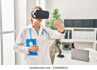 Young Blonde Woman Wearing Doctor Uniform Using Touchpad And Vr Goggles At Clinic