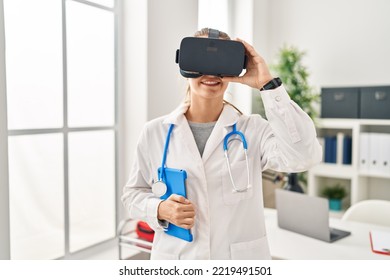 Young Blonde Woman Wearing Doctor Uniform Using Touchpad And Vr Goggles At Clinic