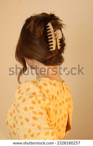 Young blonde woman wearing hair up in claw clip. Summer hairstyle. Trendy hairstyle. Yellow summer dress. Beige claw clip. 
