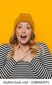 Young blonde woman wearing hat expressing surprise at camera isolated over yellow background