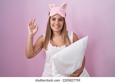Young blonde woman wearing pyjama hugging pillow smiling positive doing ok sign with hand and fingers. successful expression.  - Shutterstock ID 2205827759