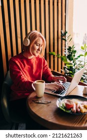 Young Blonde Woman Wearing Red Casual Sweater In Cafe Working On The Laptop Computer And Drinking Coffe Lifestyle