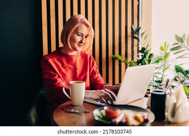 Young Blonde Woman Wearing Red Casual Sweater In Cafe Working On The Laptop Computer And Drinking Coffe Lifestyle