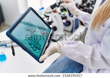 Young blonde woman wearing scientist uniform looking embryion images at laboratory