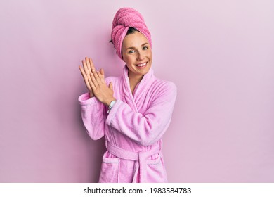 Young blonde woman wearing shower towel cap and bathrobe clapping and applauding happy and joyful, smiling proud hands together 
