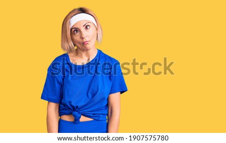 Young blonde woman wearing sportswear making fish face with lips, crazy and comical gesture. funny expression. 