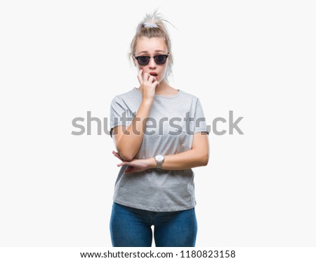 Young blonde woman wearing sunglasses over isolated background looking stressed and nervous with hands on mouth biting nails. Anxiety problem.
