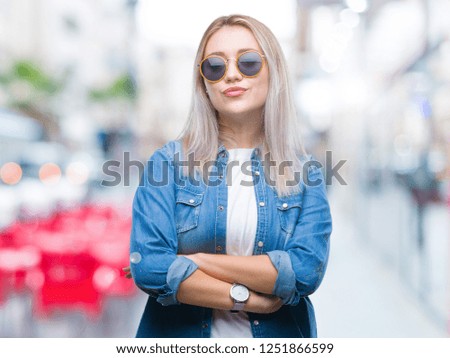 Young blonde woman wearing sunglasses over isolated background happy face smiling with crossed arms looking at the camera. Positive person.