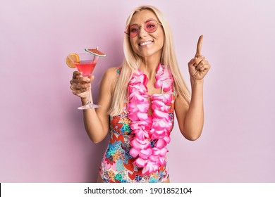 Young blonde woman wearing swimsuit and hawaiian lei drinking cocktail smiling with an idea or question pointing finger with happy face, number one 