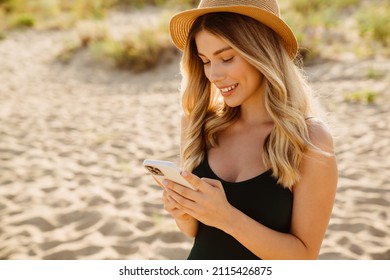 Young blonde woman wearing swimsuit smiling and using cellphone on beach - Powered by Shutterstock