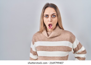 Young Blonde Woman Wearing Turtleneck Sweater Over Isolated Background In Shock Face, Looking Skeptical And Sarcastic, Surprised With Open Mouth 