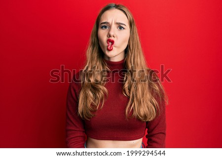 Young blonde woman wearing turtleneck sweater making fish face with lips, crazy and comical gesture. funny expression. 