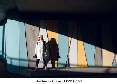 Young blonde woman in white winter coat standing against colorful wall with geometric pattern under the bridge in Norway. Urban background. Pedestrian tunnel. Art concept. - Powered by Shutterstock