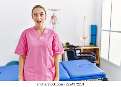 Young Blonde Woman Working At Pain Recovery Clinic Afraid And Shocked With Surprise Expression, Fear And Excited Face. 