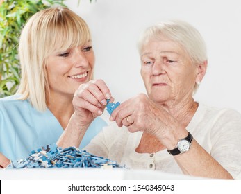 a young blonde women, a nurse or a caregiver, play some games with an old grey haired women or grandmother in a wheelchair and they have fun at her work in care
